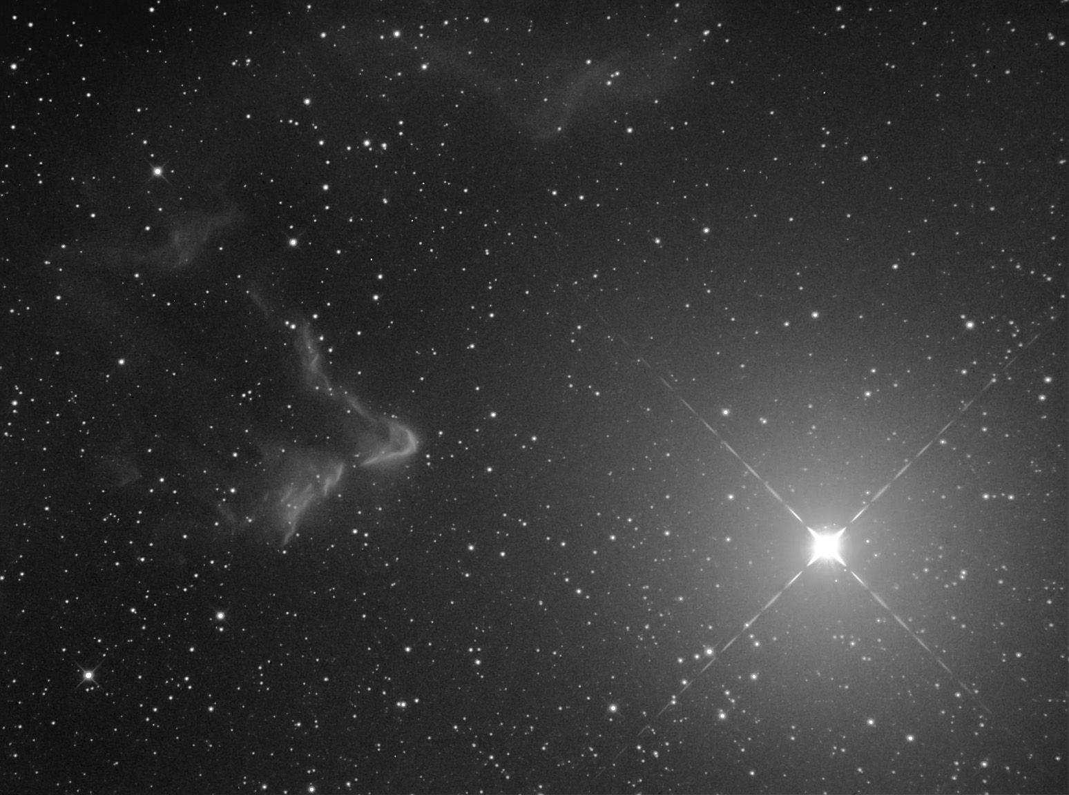 Black-and-white wisps of nebulosity to the left of a very bright star with diffraction spikes