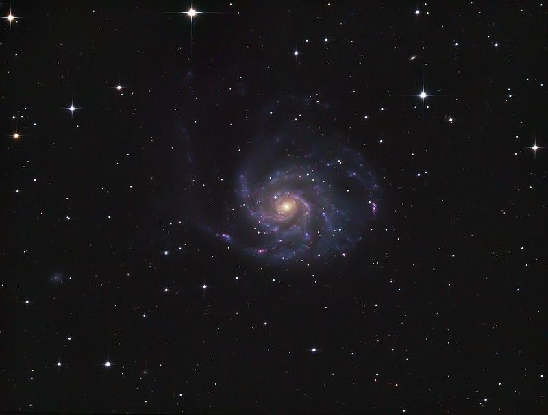 Face-on spiral galaxy with blue arms and a yellowish core, offset to the lower right of a star field