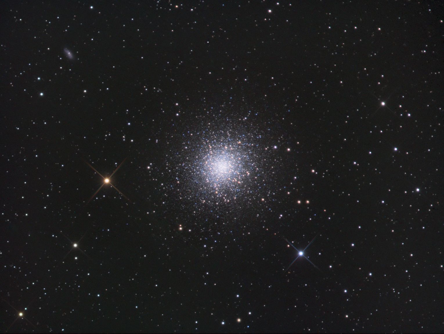 Dense spherical globular cluster of white stars near the centre of a star field, with a bright orange star at left