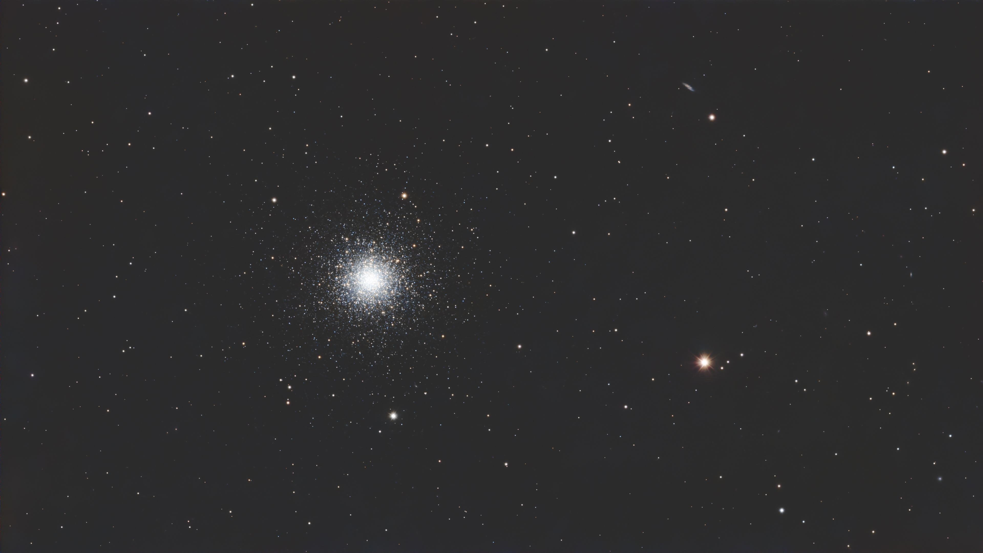 Bright compact globular cluster of white stars at the centre of a sparse star field, with an orange star nearby