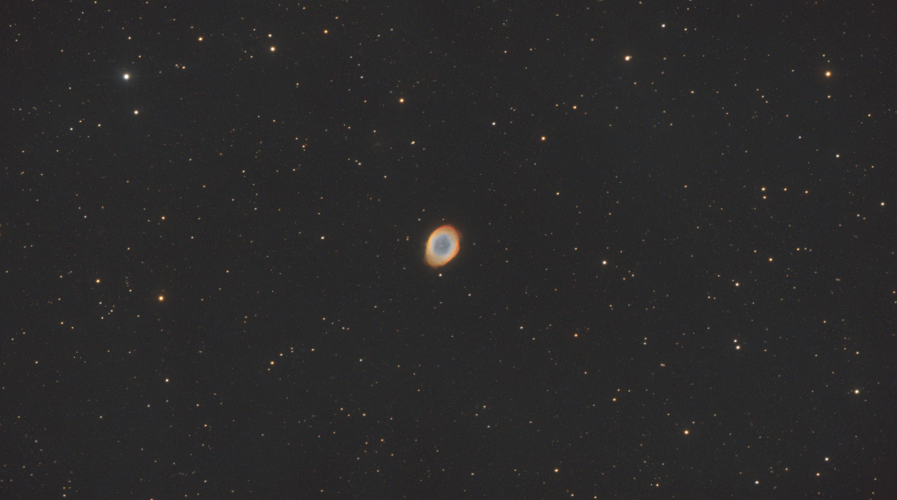Small glowing ring of blue and orange gas near the centre of a wide star field