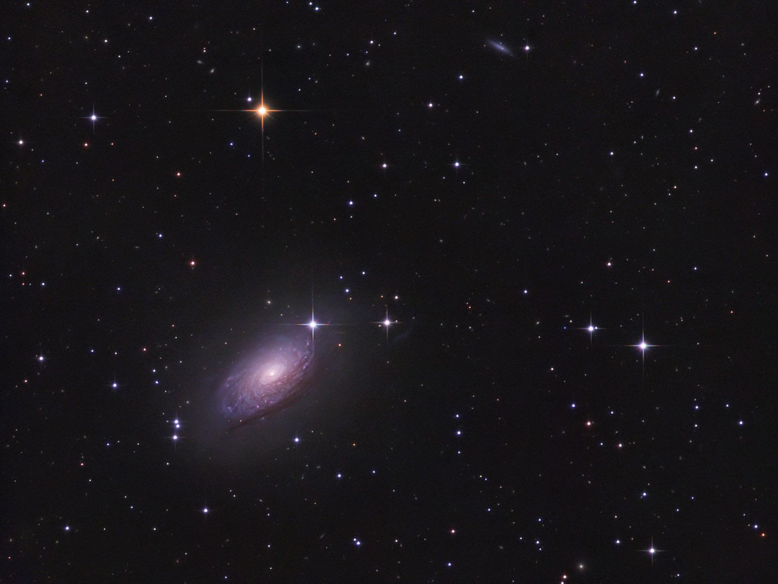 Tilted spiral galaxy with a bright core and mottled purple-blue arms among bright foreground stars