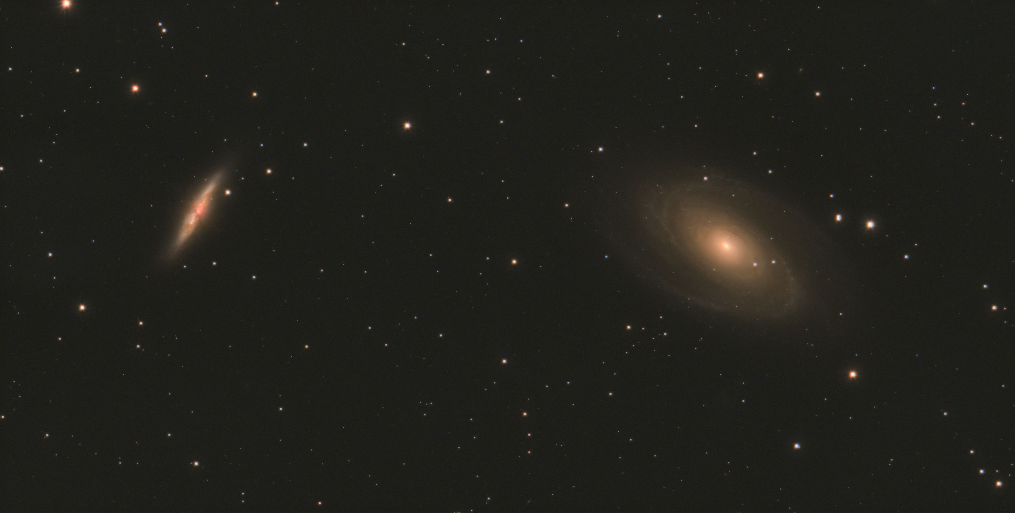 Two galaxies in one field: a tilted edge-on galaxy at left and a larger oval spiral galaxy with a warm core at right