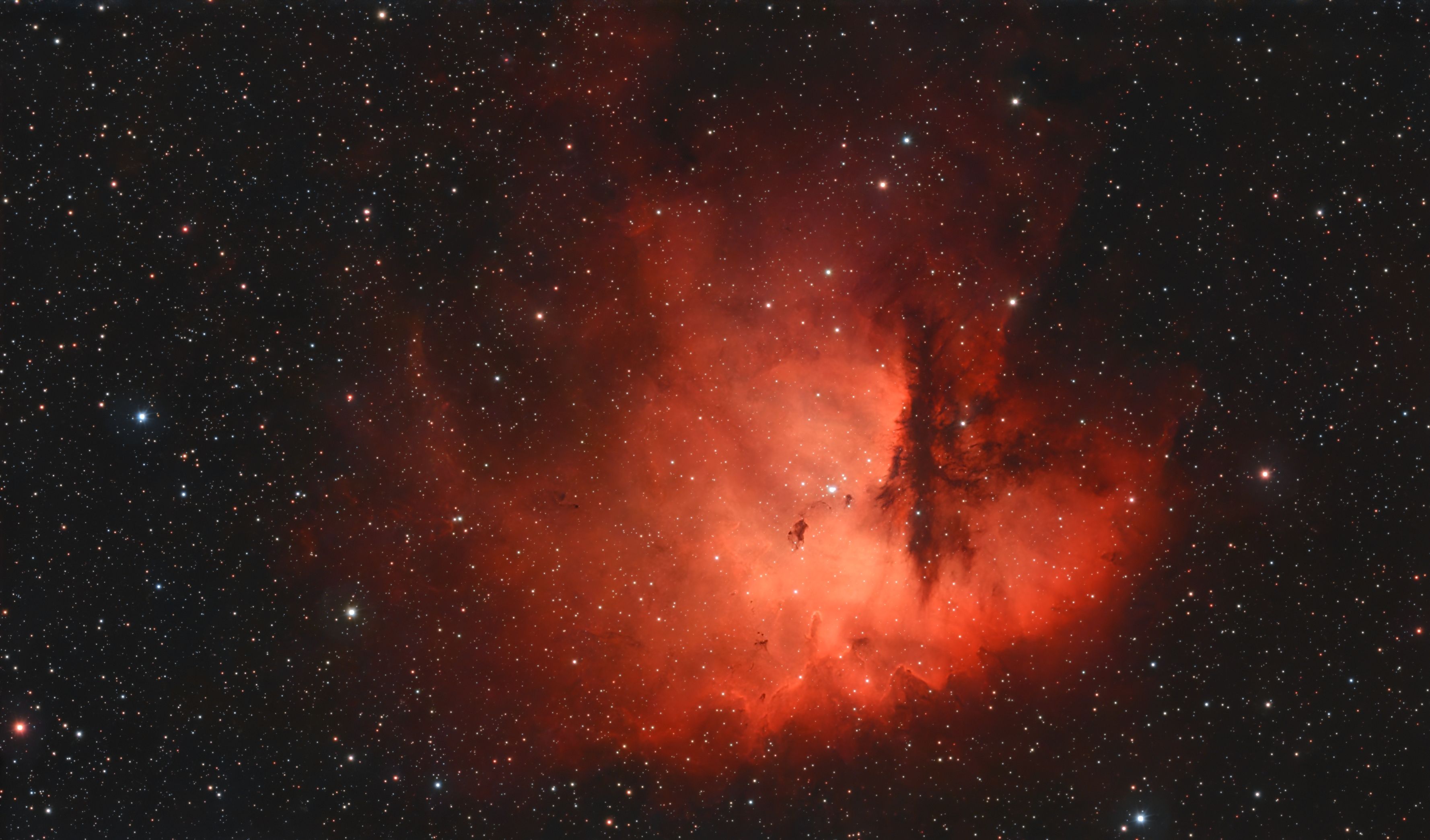 Bright red emission nebula with dark dust lanes cutting into it from the right, filled with stars