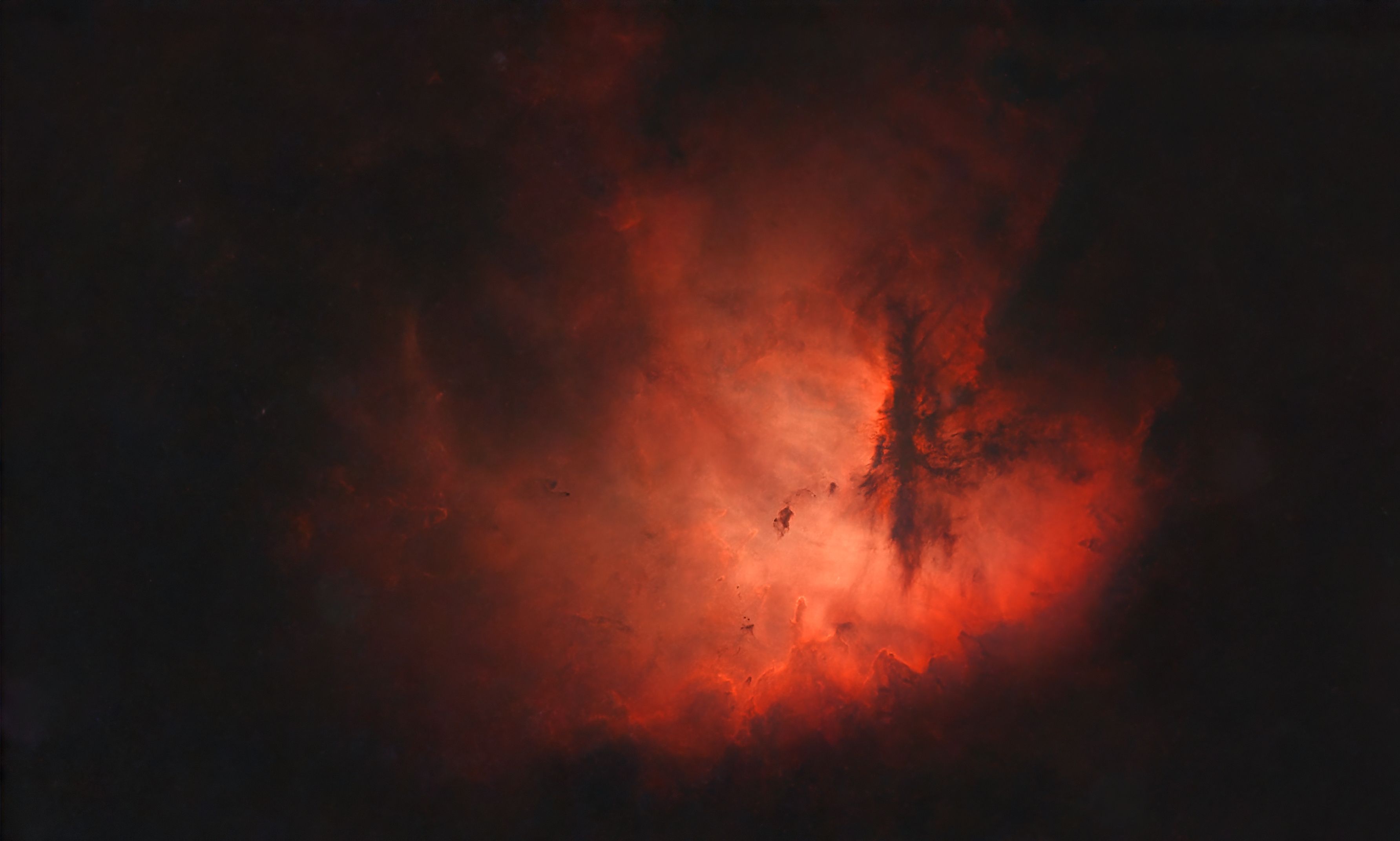 Bright red emission nebula with dark dust lanes, shown in a starless version with the stars removed
