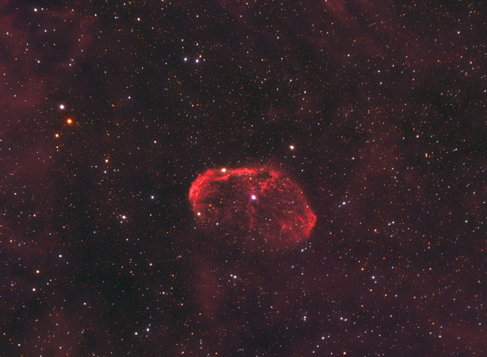 Red crescent-shaped shell of glowing gas with filamentary structure in a dense star field