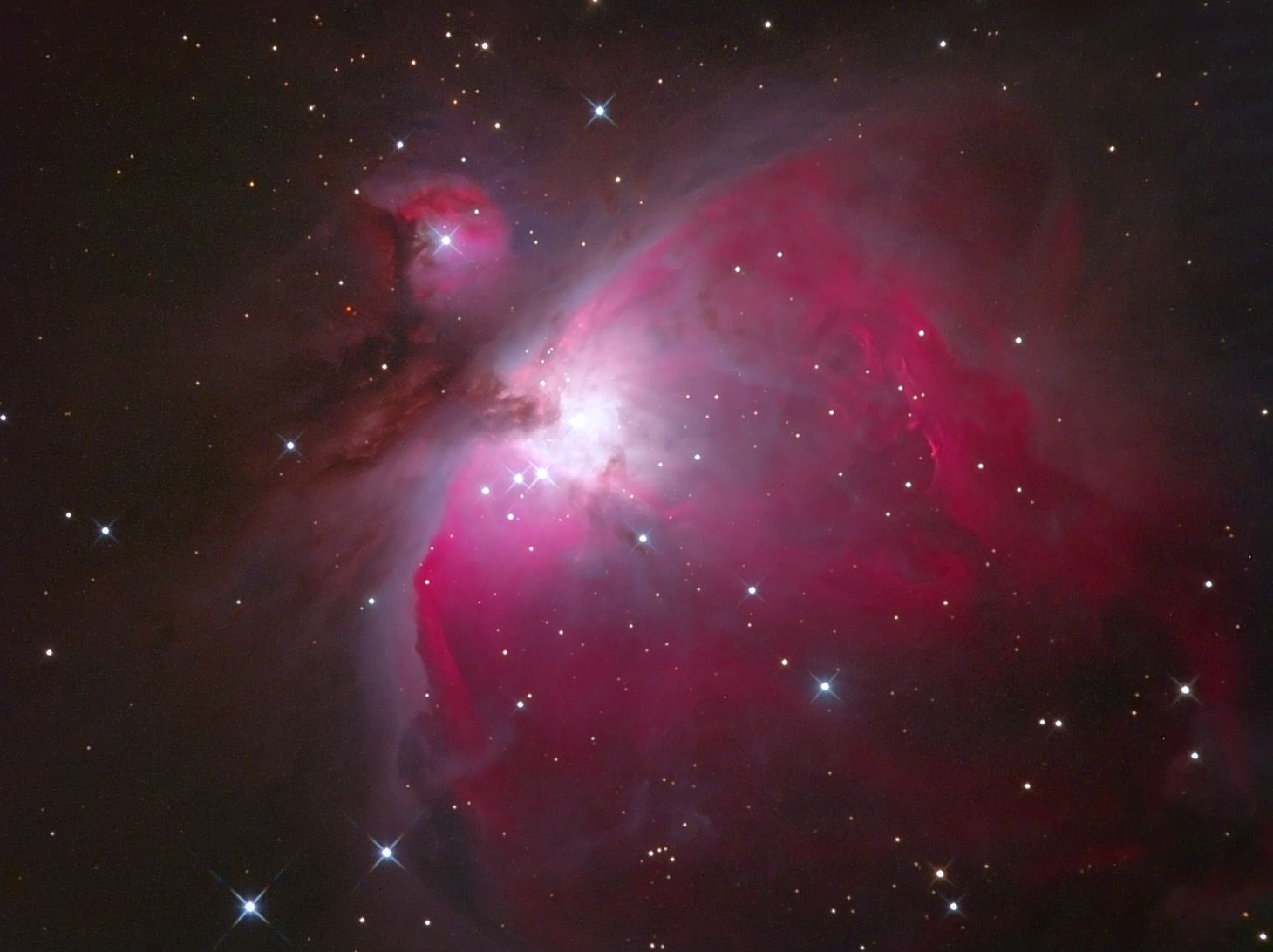 Bright pink and white glowing gas clouds with dark dust lanes and a brilliant core, with a smaller nebula at upper left