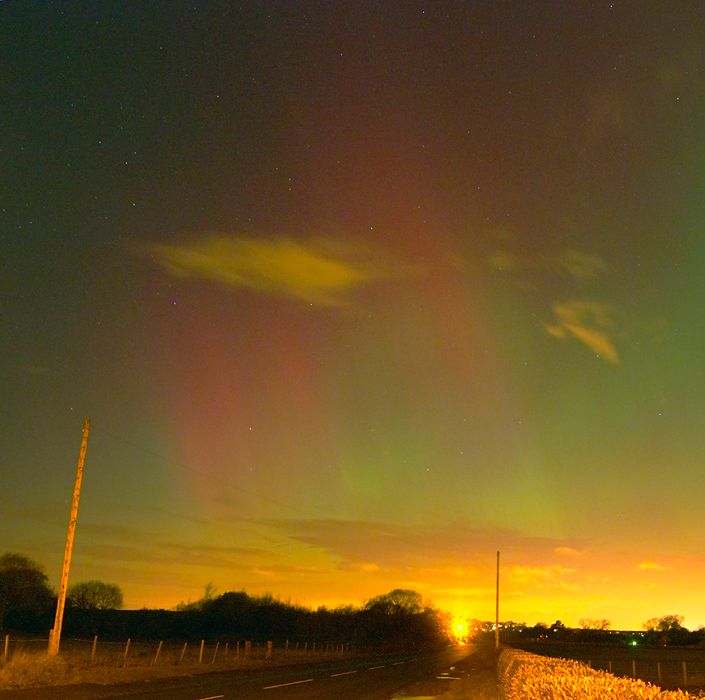 Red and green aurora over a country road with a telegraph pole and a bright light on the horizon